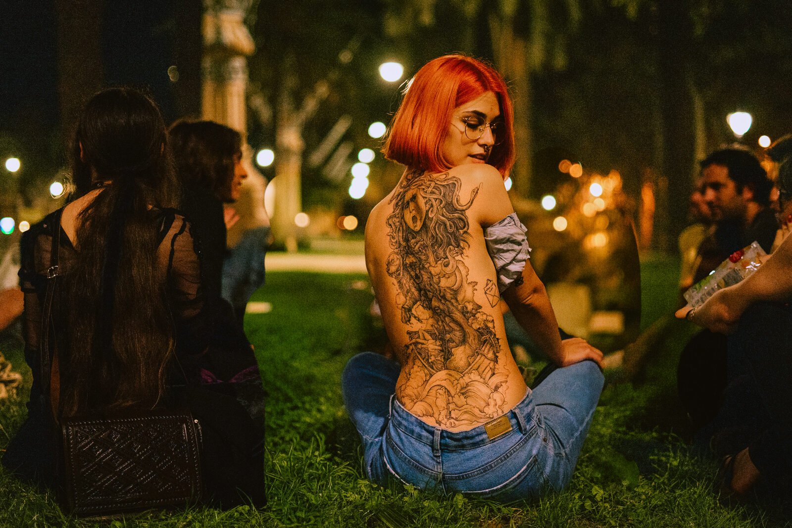 Espalda tatuada en plaza nocturna, luz cálida