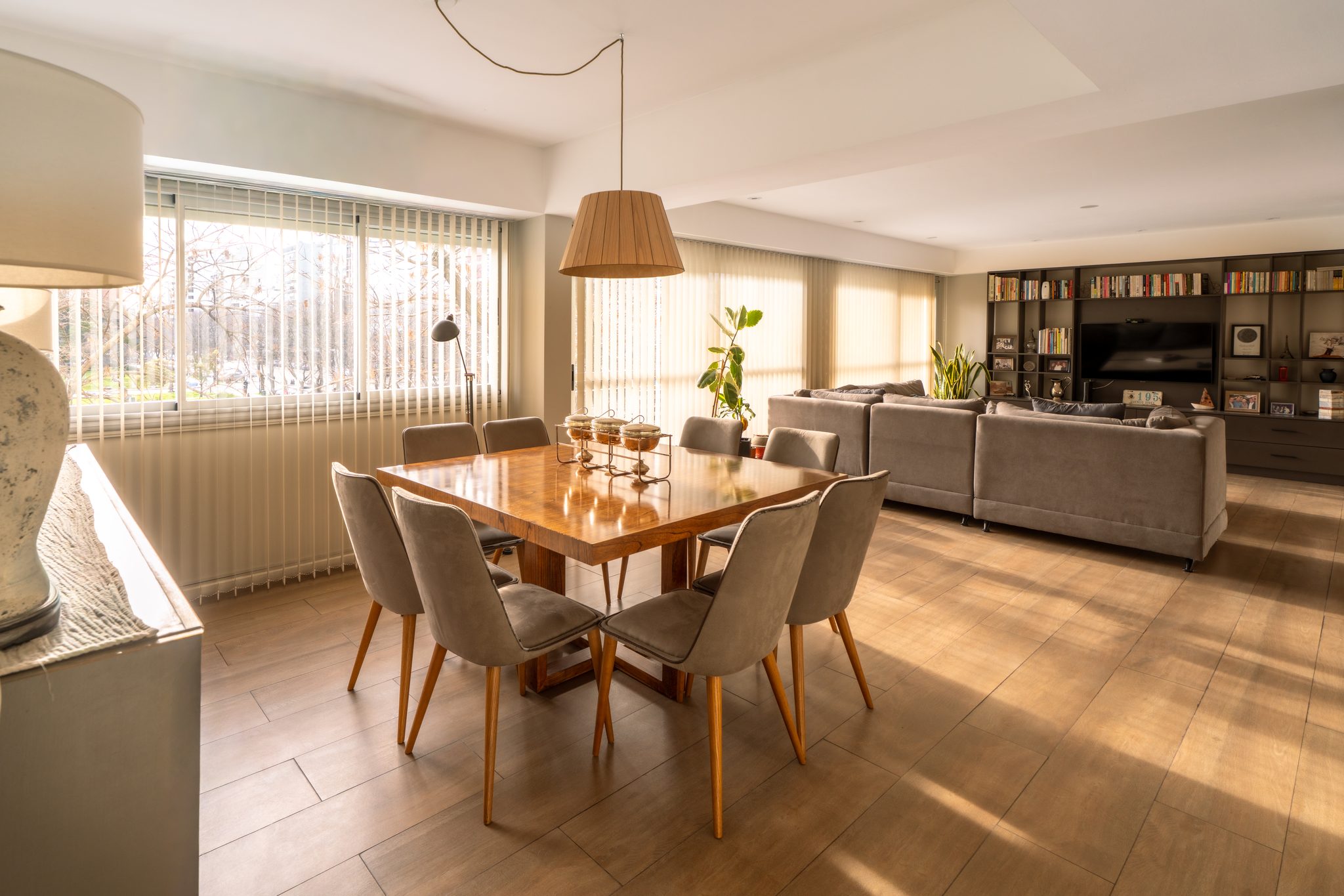 Living-comedor integrado con biblioteca de obra, luz de tarde sobre piso de madera