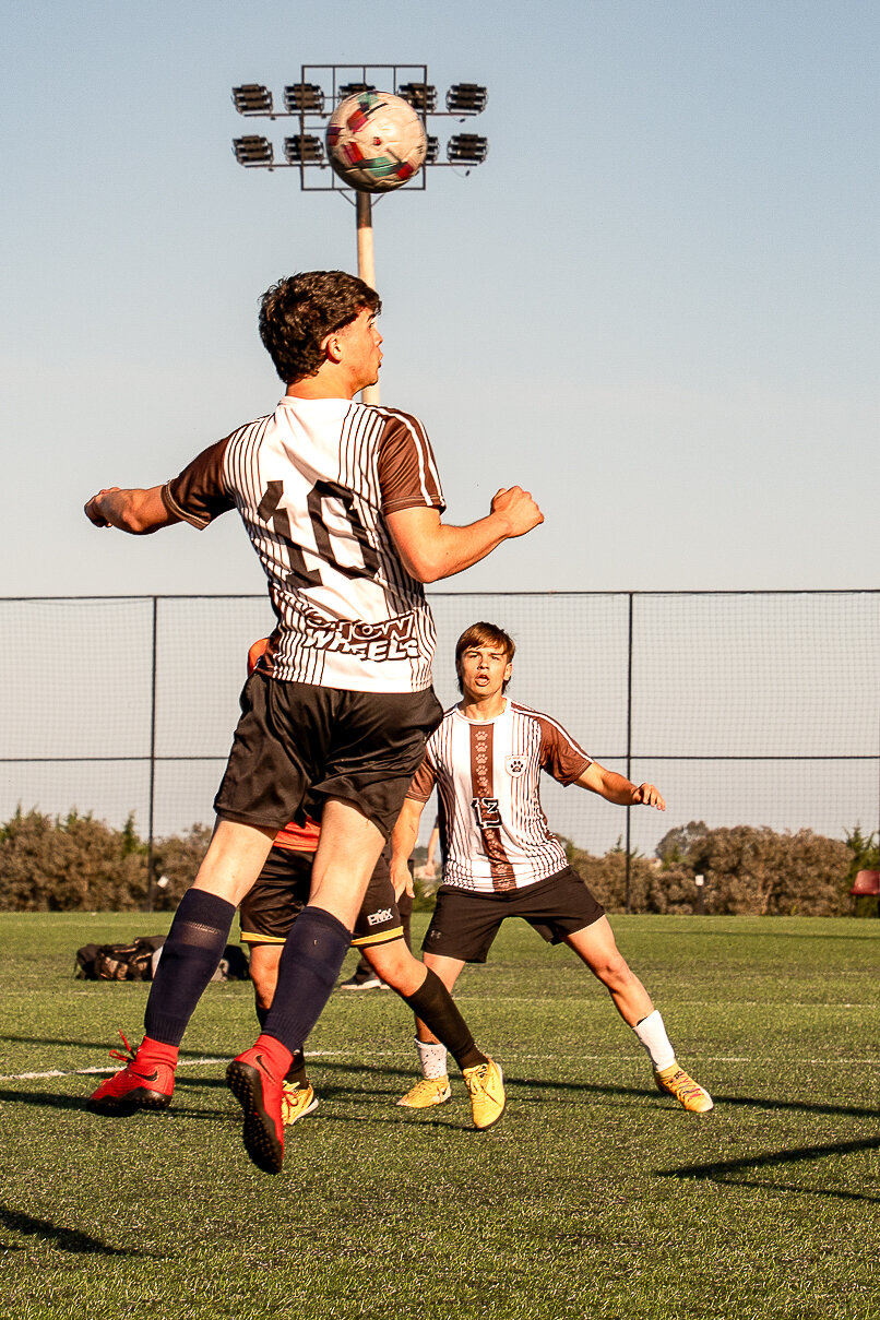 Jugador de camiseta rayada cabeceando la pelota bajo las torres de luz