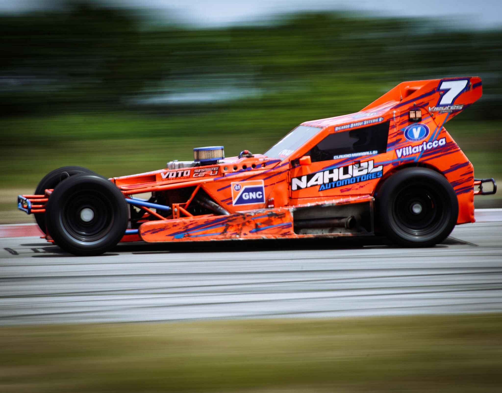 Auto de carrera naranja número 7 a toda velocidad, fotografiado en paneo